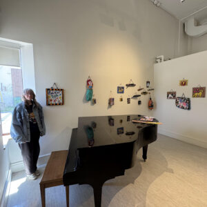 image of woman with long light hair standing next to folk art displayed on a gallery wall.